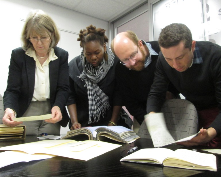 Figure 2. From left, retired head of Special Collections, University of Cape Town Library, Leslie Hart, together with student Treasure Redmond, project director, Adrian S. Wisnicki, and project scholar, Jared McDonald, examining Livingstone letters in 2013. Copyright Angela Aliff, CC BY-NC 3.0. (https://creativecommons.org/licenses/by-nc/3.0/)
